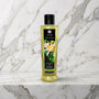 Fles groene thee massageolie met zwart etiket op een marmeren plank, Shunga Organica