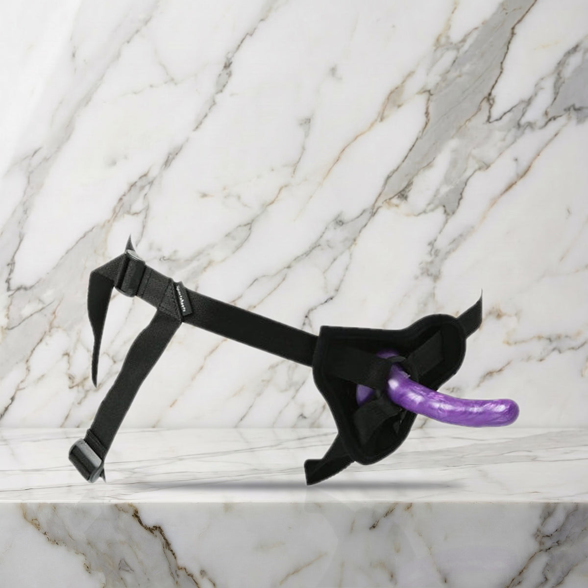 Zwart verstelbaar harnas met paarse siliconen dildo op een marmeren plank, Sportsheets