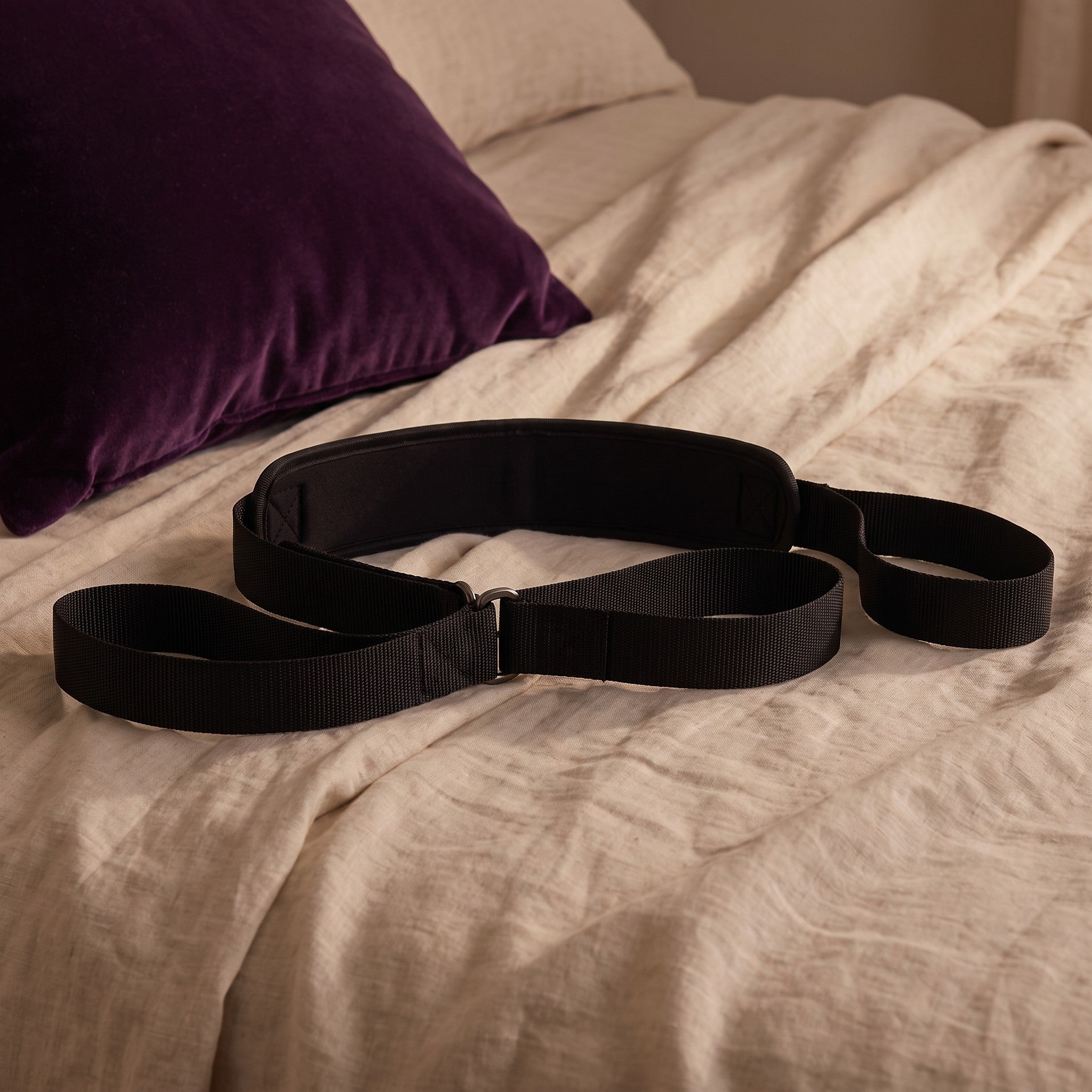 Sfeerbeeld: zwarte Sportsheets strap op een bed met creme linnen naast een paars kussen