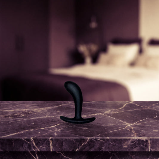 Sfeerbeeld: zwarte Star Yed 1 buttplug op een donker marmeren nachtkastje in een slaapkamer