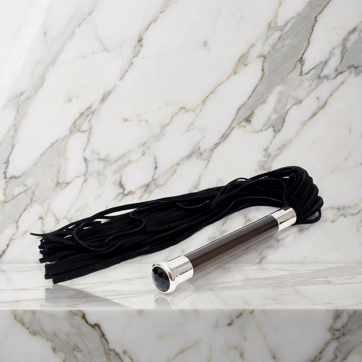Zwarte suède flogger met glazen handvat en kristal op een marmeren plank