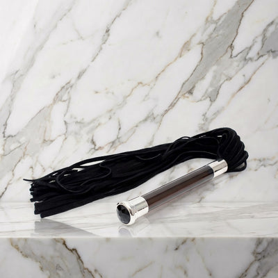 Zwarte suède flogger met glazen handvat en kristal op een marmeren plank