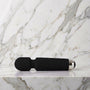 Zwarte Super Wand wandmassager klein formaat liggend op een lichte marmeren plank