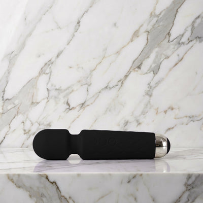 Zwarte Super Wand wandmassager klein formaat liggend op een lichte marmeren plank