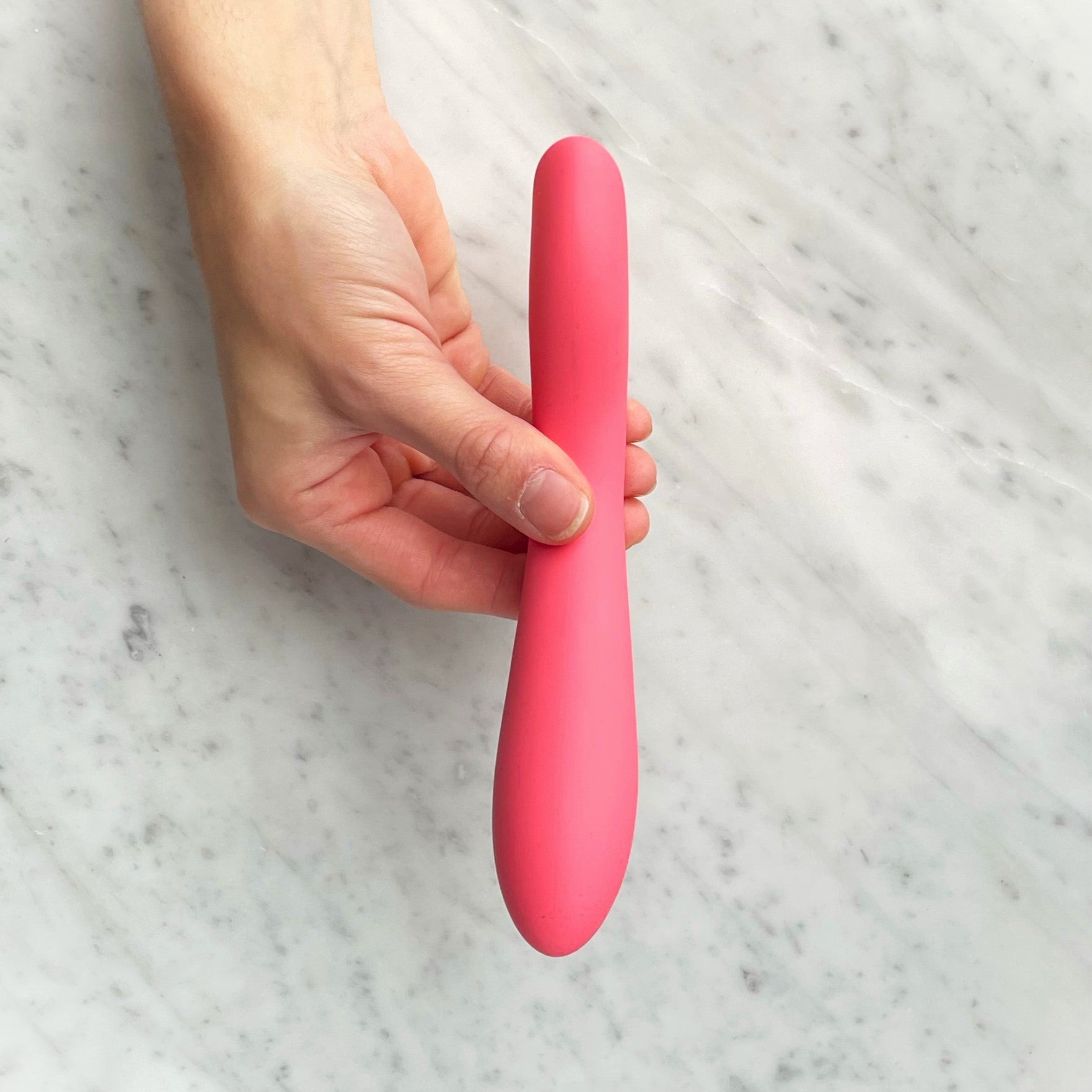 Koraalroze slanke vibrator van de Gentle Sensations Kit rechtop in een hand