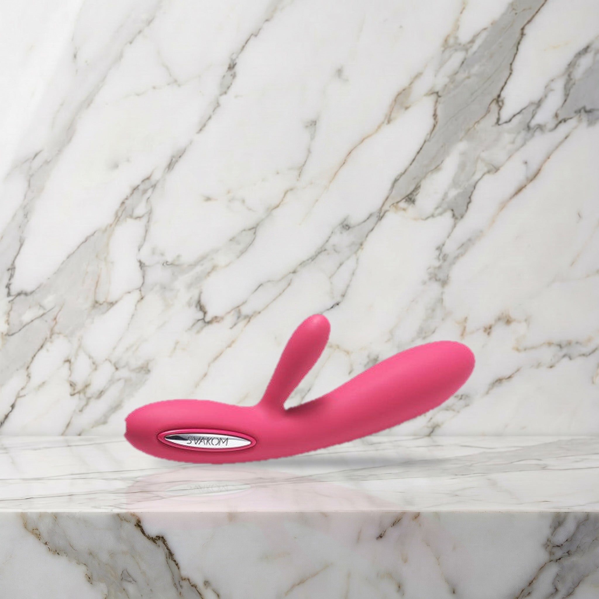 Roze rabbit vibrator met zilverkleurig bedieningsvlak liggend op een marmeren plank, Svakom Lester