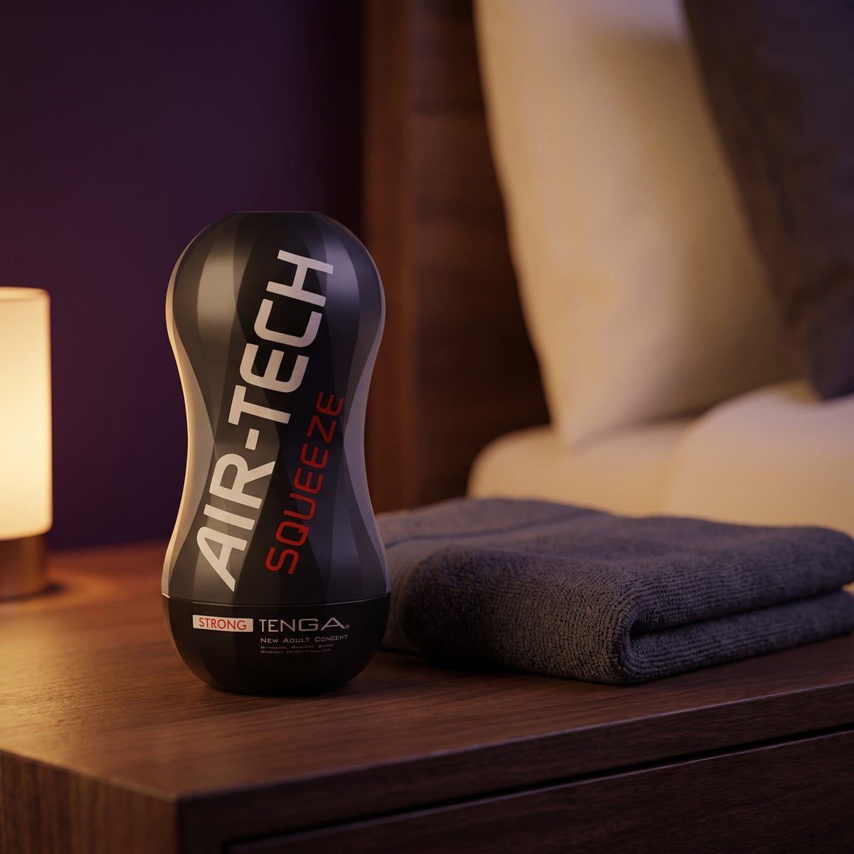 Sfeerbeeld: de Air Tech Squeeze Strong op een nachtkastje naast een handdoek, van Tenga
