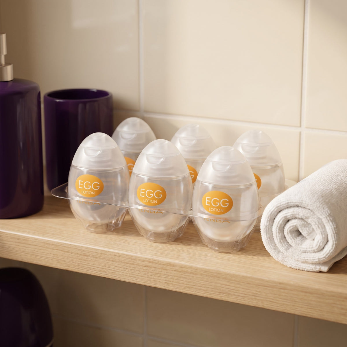 Sfeerbeeld: zes flesjes Tenga Egg Lotion op een badkamerplank naast een opgerolde handdoek