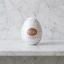 Wit masturbator-ei Egg Silky II met zilveren lijnen op een marmeren plank, Tenga