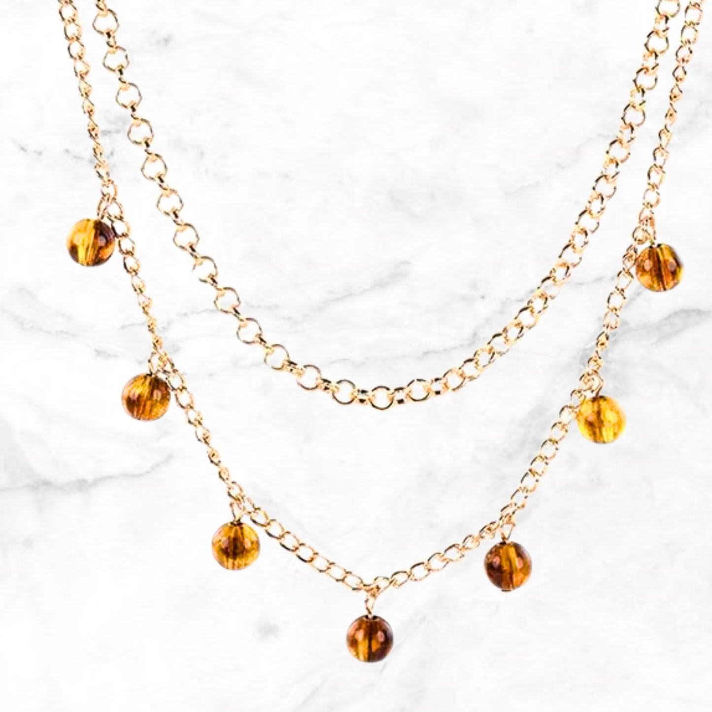 Close-up dubbele goudkleurige ketting met amberkleurige kristallen hangers