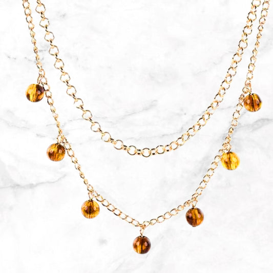 Close-up dubbele goudkleurige ketting met amberkleurige kristallen hangers
