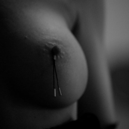 Sexy tepelkwastjes van leer, zwart-witfoto van borst met tepelklemmen met metalen gewichtjes.