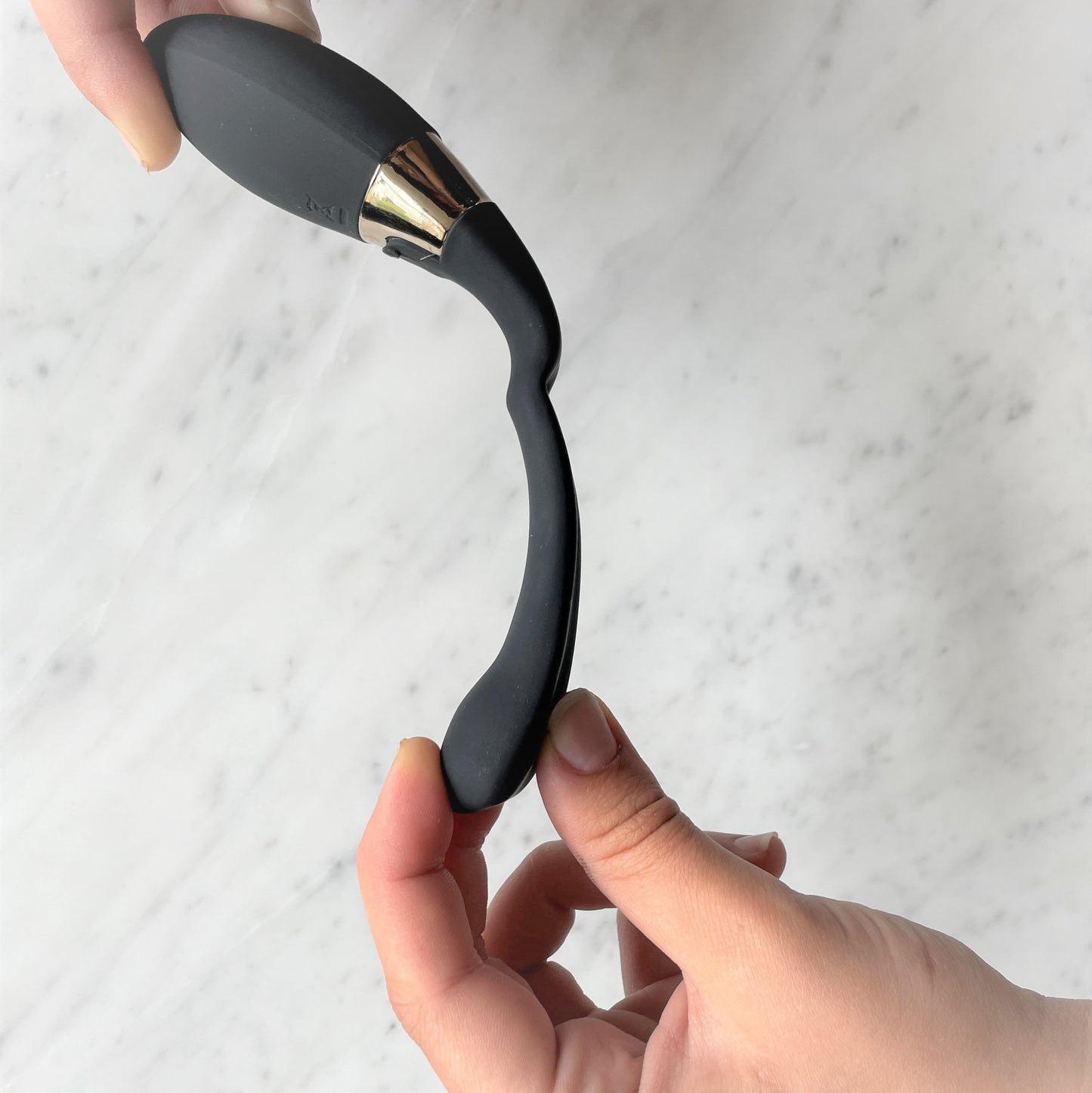 Handen buigen Lelo Tiani Duo open op marmeren ondergrond, toont flexibel siliconen