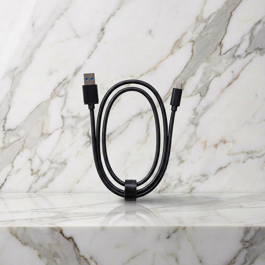 Zwarte gevlochten USB-C oplaadkabel, opgerold op een marmeren plank