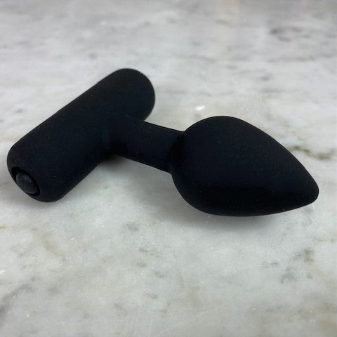 Kleine zwarte buttplug XS liggend op grijs marmer, zijaanzicht met de T-vormige voet