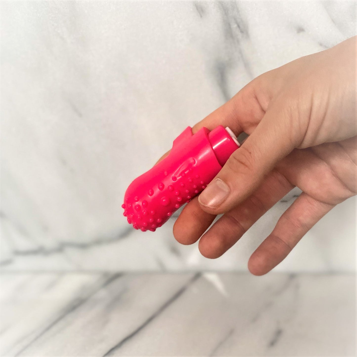 Hand met roze Screaming O fingervibrator met nopjesstructuur tegen marmeren achtergrond