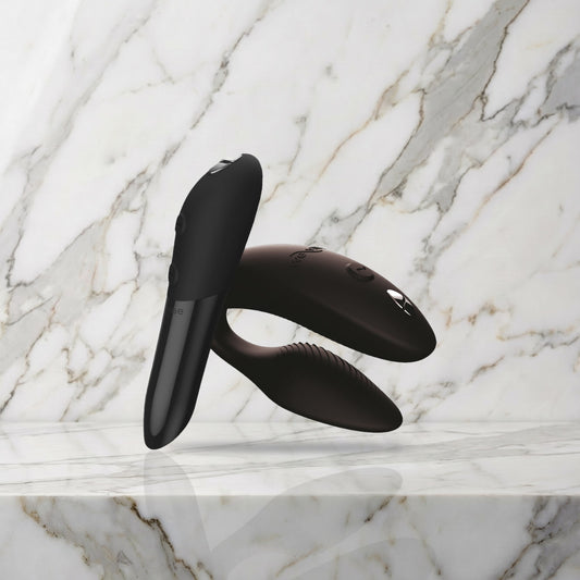 Zwarte Sync 2 koppelvibrator en Tango X mini vibrator op een marmeren plank, We-Vibe
