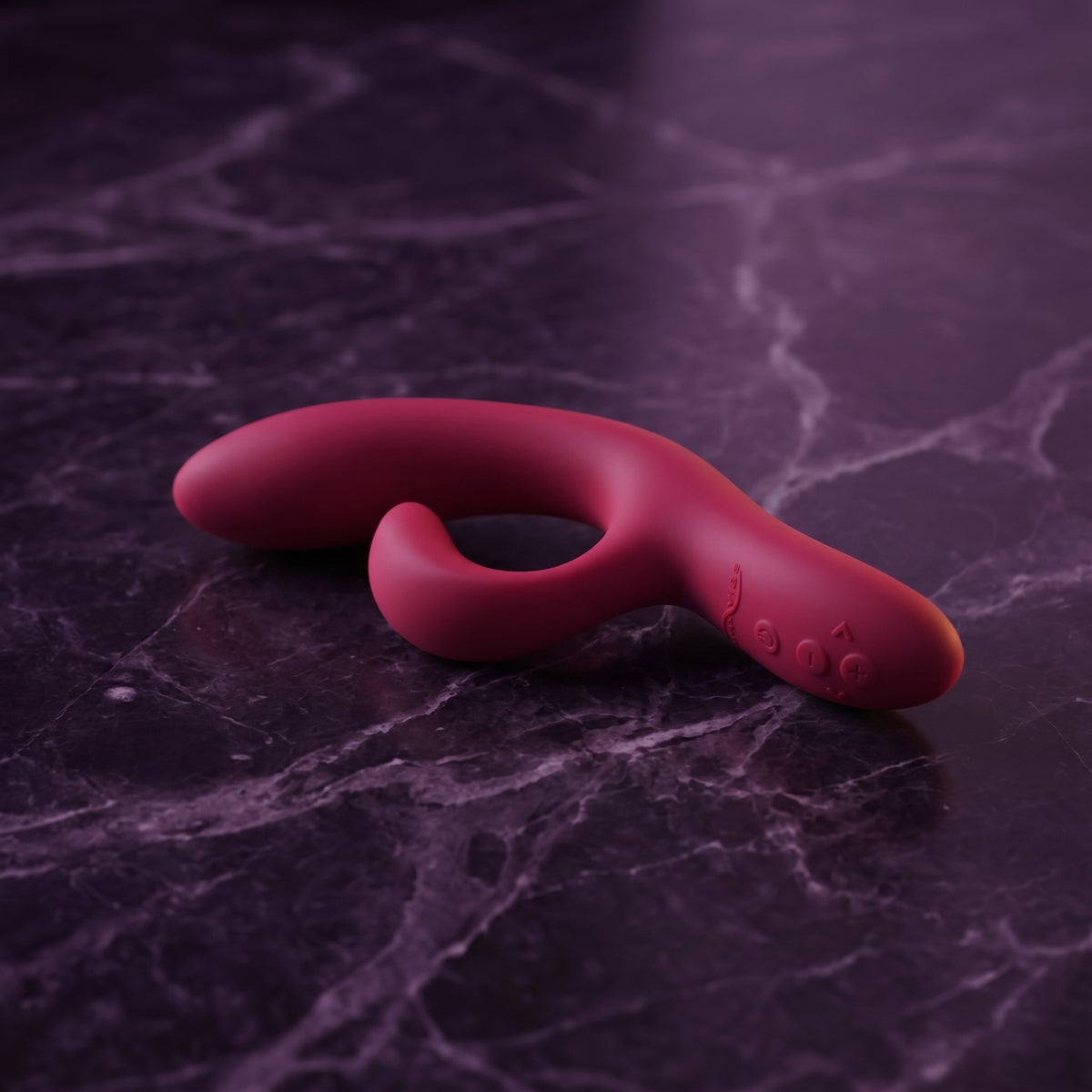 Sfeerbeeld: We-Vibe Nova 2 in roze-rood liggend op donkerpaars marmer in gedempt licht