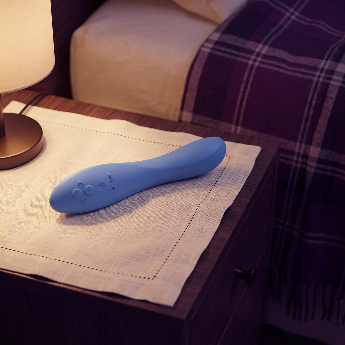 Sfeerbeeld: de blauwe Rave 2 op een nachtkastje bij lamplicht naast het bed, van We-Vibe