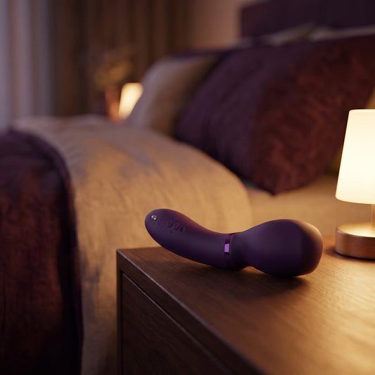 Sfeerbeeld: We-Vibe Wand 2 op een houten nachtkastje bij een lamp in avondlicht