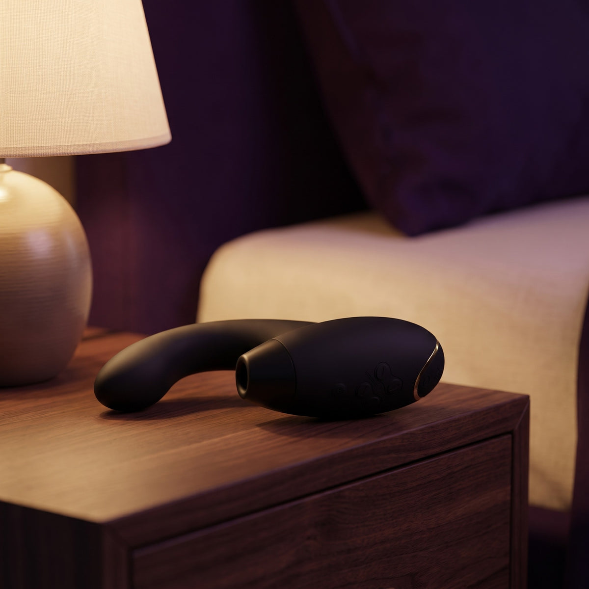 Sfeerbeeld: zwarte Womanizer Duo 2 op een houten nachtkastje naast een brandende lamp
