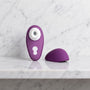 Paarse luchtdrukvibrator met wit mondstukje en los kapje op een marmeren plank, Liberty 2 van Womanizer