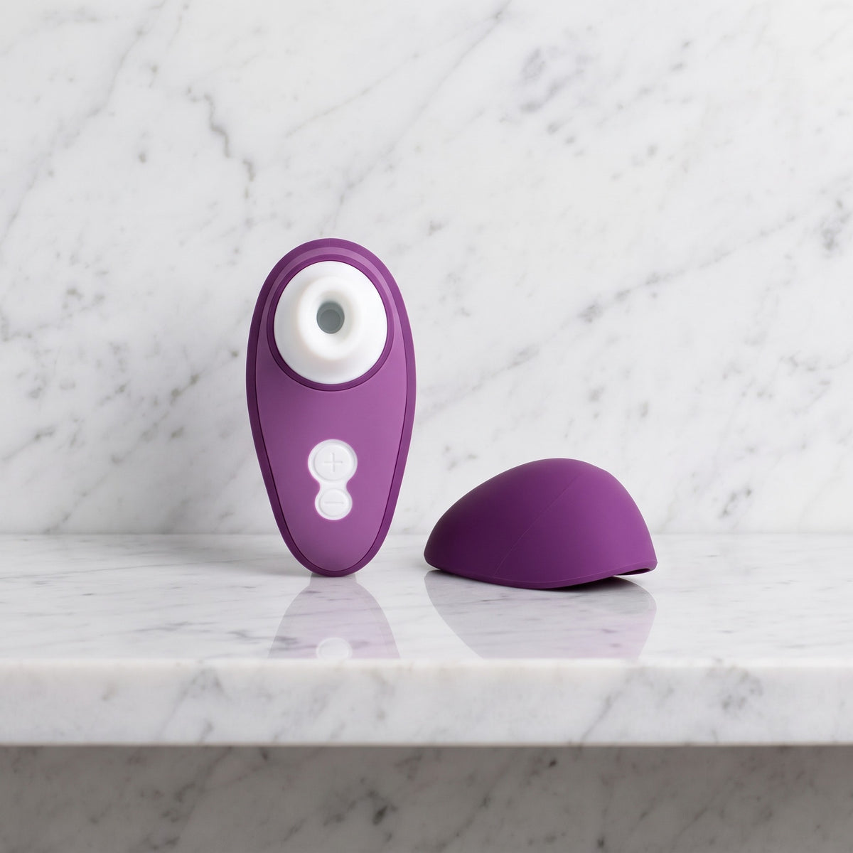 Paarse luchtdrukvibrator met wit mondstukje en los kapje op een marmeren plank, Liberty 2 van Womanizer