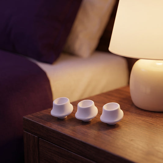 Sfeerbeeld: drie witte mondkapjes op een houten nachtkastje naast een lamp