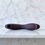 Womanizer OG in aubergine, gebogen G-spotvibrator met luchtdrukmondje, op een marmeren plank