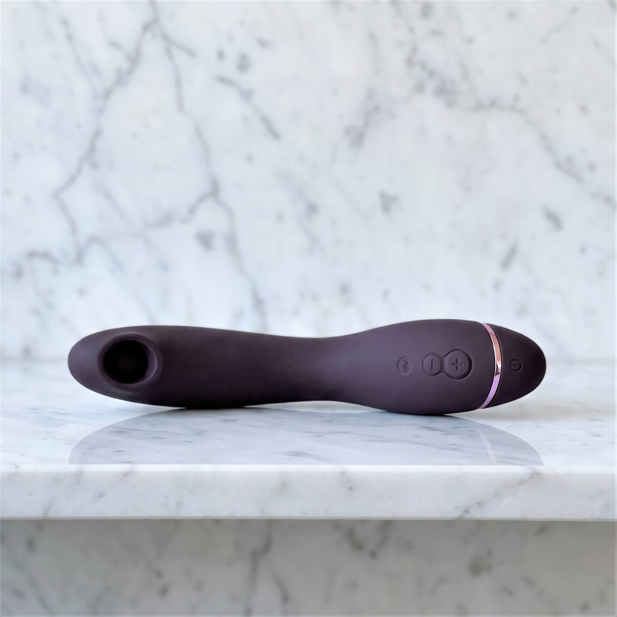 Womanizer OG in aubergine, gebogen G-spotvibrator met luchtdrukmondje, op een marmeren plank