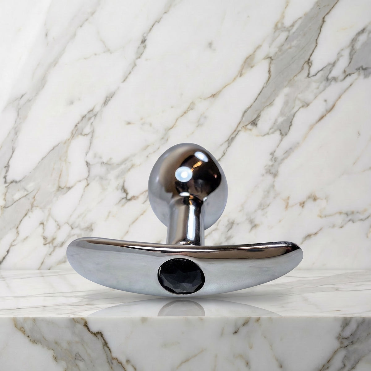 Zilverkleurige metalen buttplug met zwart siersteentje op een marmeren plank, maat S