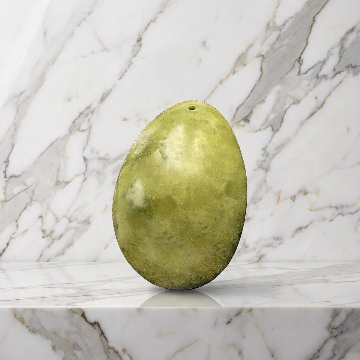 Groot lichtgroen jade yoni ei met gaatje in de kop op een marmeren plank